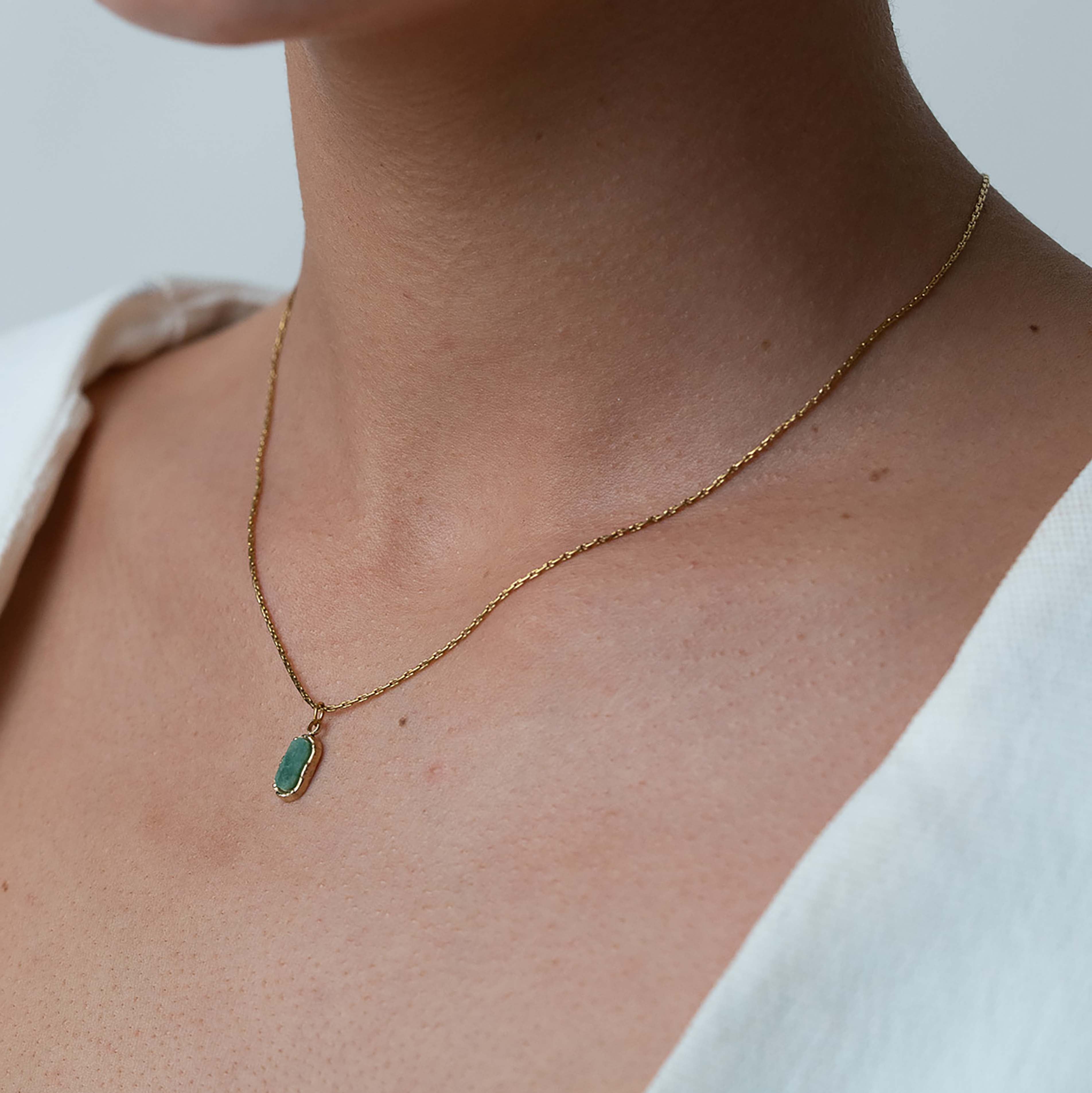Necklace with a green pendant worn by a person against a neutral background